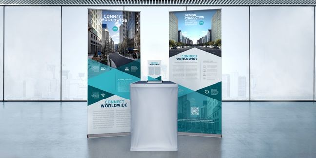 Trade show display with two banners and a covered table in a modern glass-walled room.